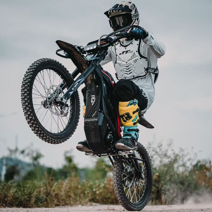 Person in motocross gear performing a wheelie on a dirt bike outdoors.