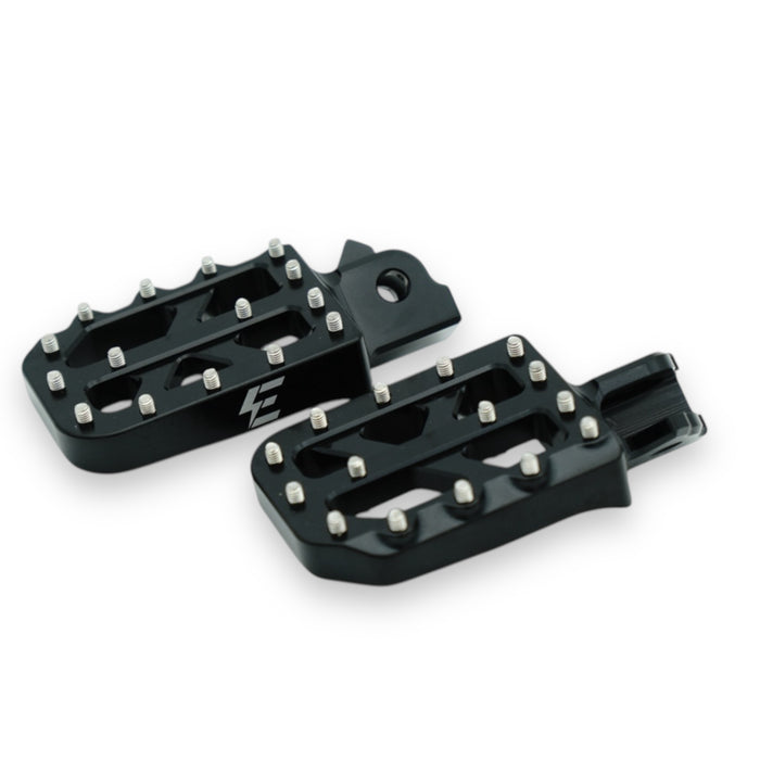 Pair of black metal motorcycle foot pegs with silver grip pins and logo