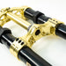 Close-up of gold motorcycle triple clamp attached to black fork tubes on white background.