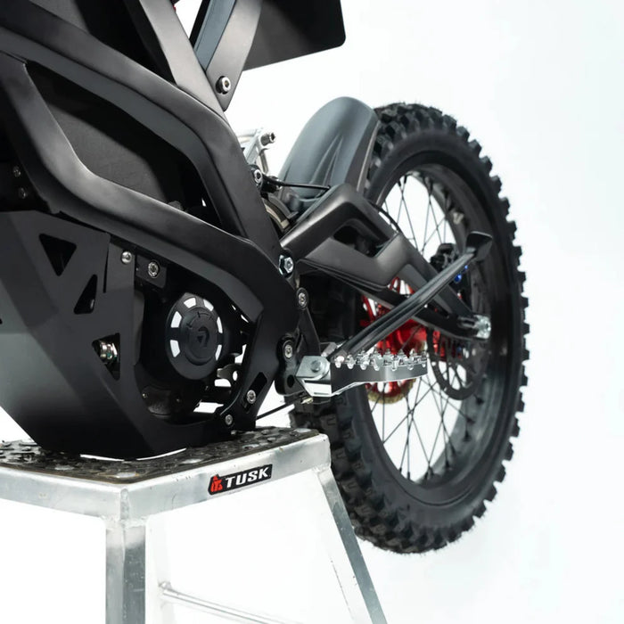 Rear section of black electric dirt bike showing swingarm, footpeg, and knobby tire