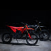 Two off-road electric dirt bikes — red and black motocross e-bikes side view
