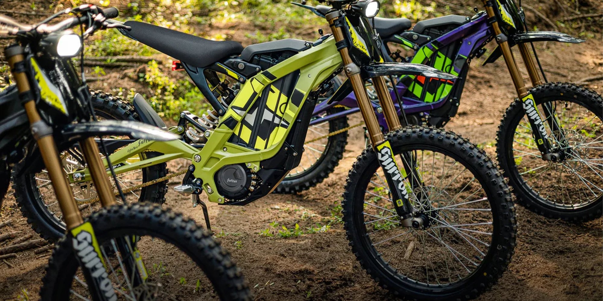 Electric dirt bikes parked in forest clearing, green and purple off-road models