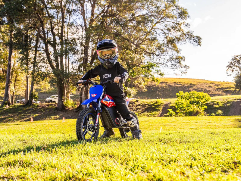 Kind auf elektrischem Mini-Offroad-Motorrad mit Schutzausrüstung auf einer Wiese im Freien